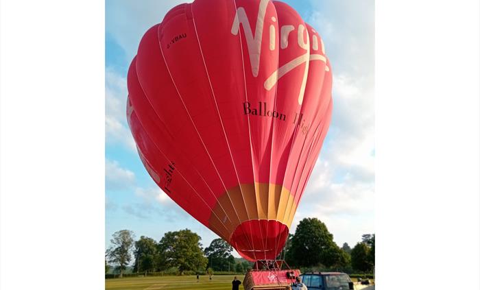 Red Virgin Balloon Flights hot air balloon preparing for take-off on a grassy launch field for a hot air balloon ride in Wales.